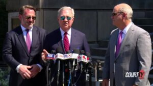 Three men in suits stand in front of microphones