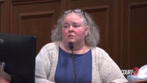 A woman in blue shirt and beige sweater testifies in court