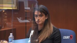 A woman sits behind plexiglass and a microphone in court