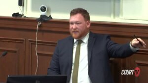 A man in a suit gestures while speaking in court