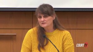 A woman in a yellow sweater testifies on the witness stand