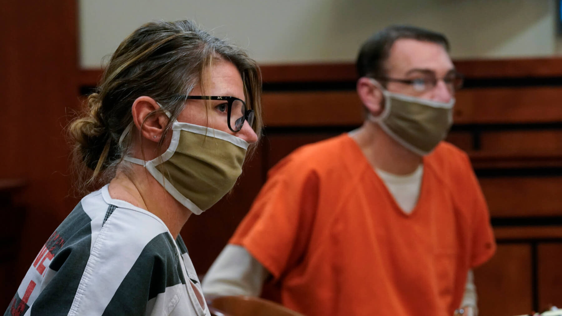A man and woman in jail uniforms and face masks sit in court