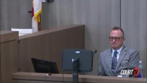 A man in a suit sits on the witness stand