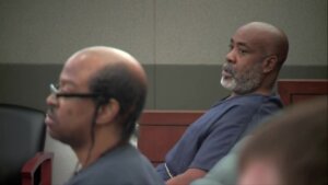 A man in blue jail issued clothing leans back in a chair in court