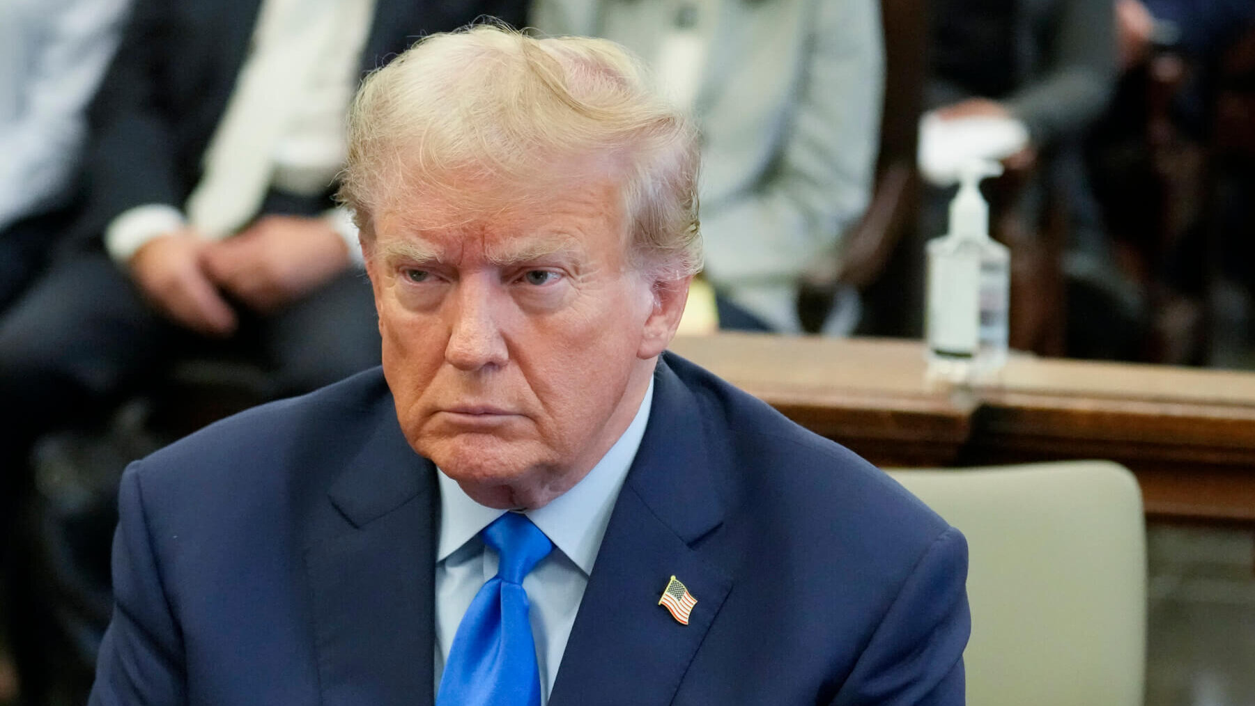 former President Donald Trump wears a blue suit and tie as he sits in a NY courtroom