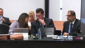 A man whispers to a woman while sitting in court