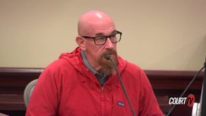 A man in a red shirt testifies in court