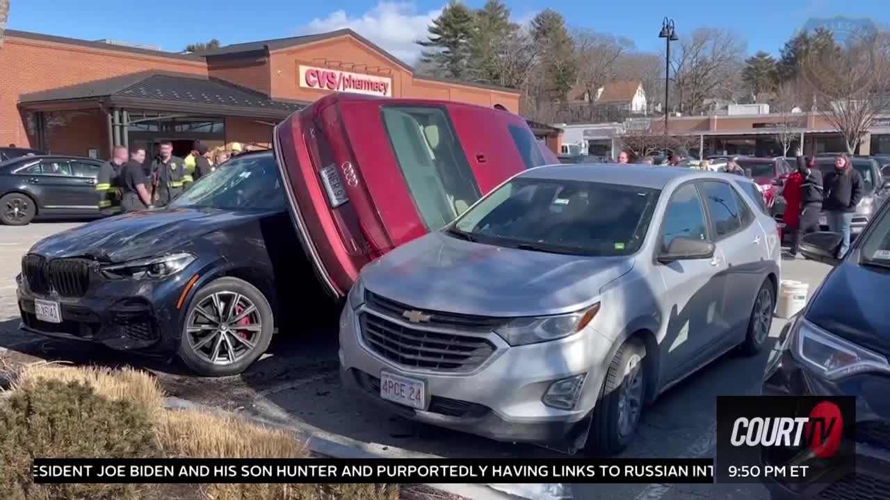 Audi wedged between 2 vehicles in a parking lot.
