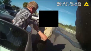 A man stands next to a deputy, whose face is obscured by a black box, outside of a cruiser in a still from bodyworn camera