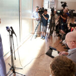 Man in a suit stands before a microphone.