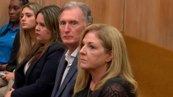 5 people on a bench in court but the focus is on an older couple who look worried.