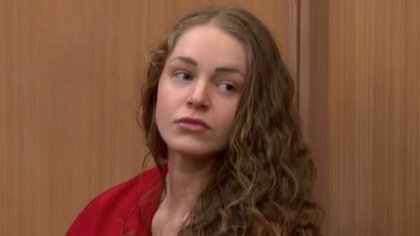 young woman with long curly hair wears an orange prison jumper in court.