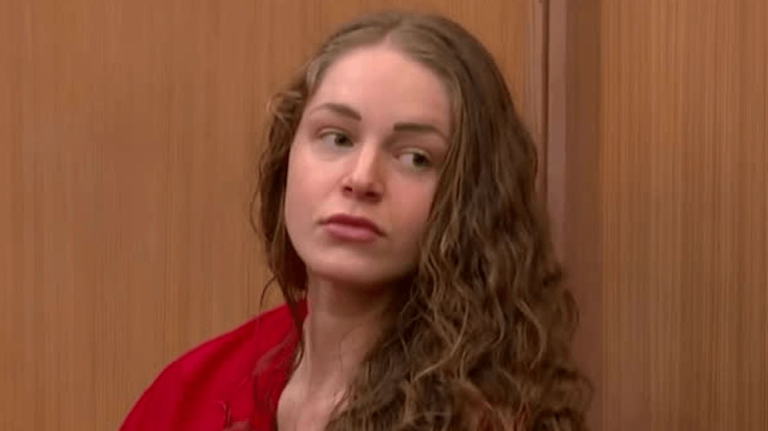 young woman with long curly hair wears an orange prison jumper in court.