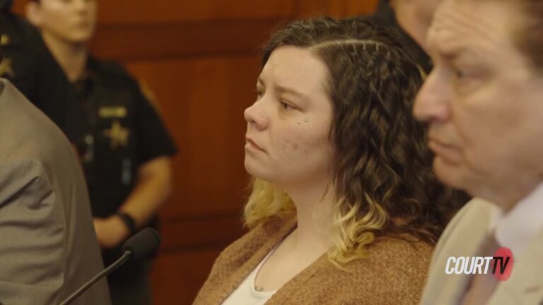 Close up profile shot of a curly haired woman standing in court wearing a brown cardigan and white scoop neck tee shirt.