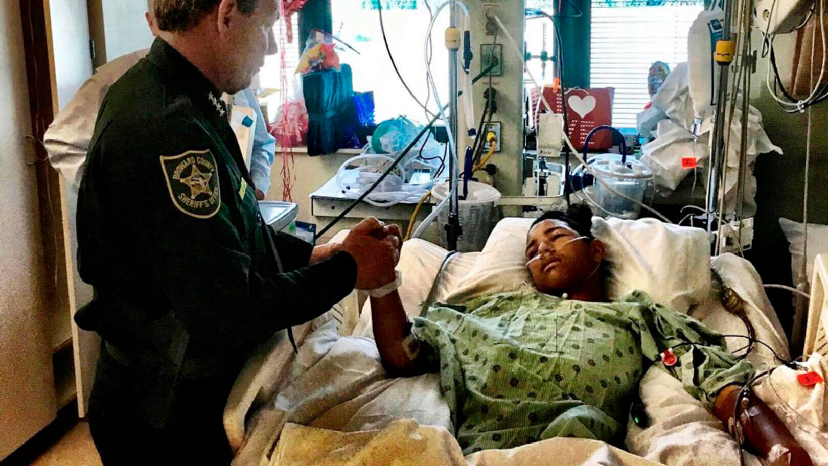 cop holds hand of patient in hospital bed