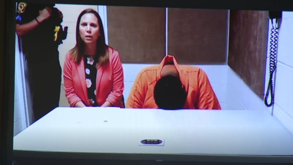 A lawyer sits next to a defendant with her head down on a table