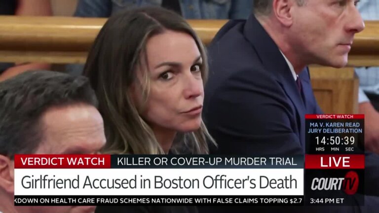 Female defendant sitting at defendant's table in court looks at the camera as her two lawyers sit on either side of her.