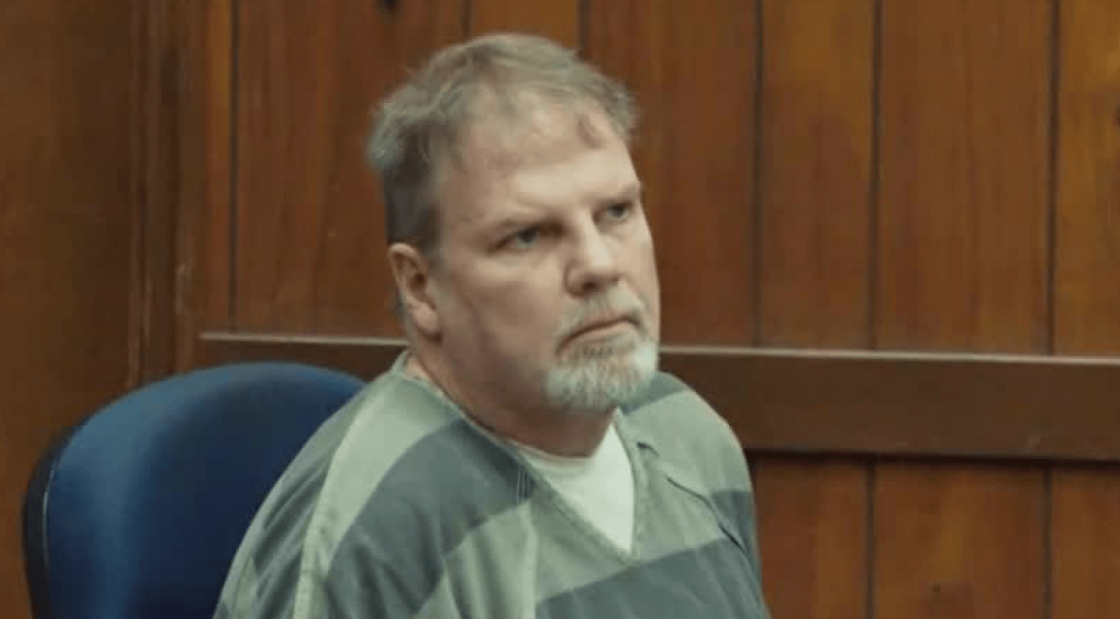 Bearded, grey-haired man in grey prison stripes.