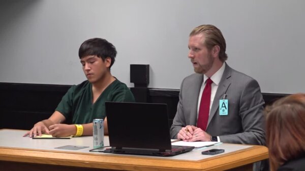 Man with dark hair sitting next to his lawyer with blond hair and red tie