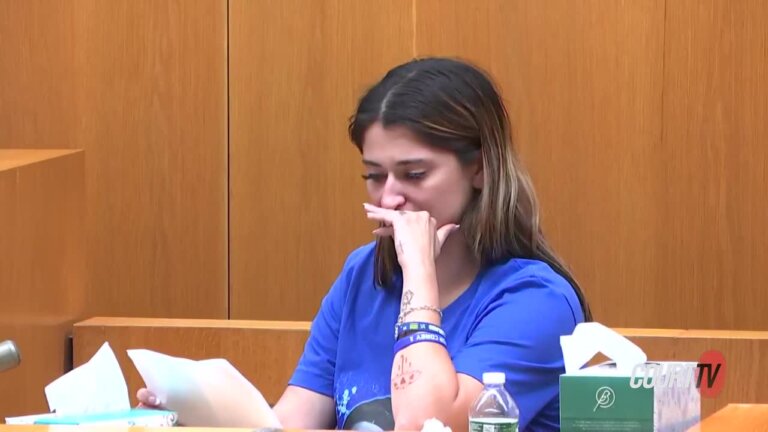 A woman holds her hand to her face while reading a letter in court.