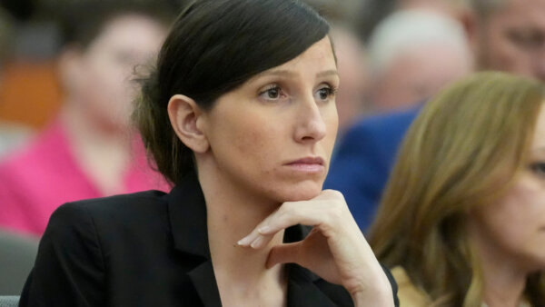 A concerned looking young woman looks on in court. She wears a black suit and a slick bun.