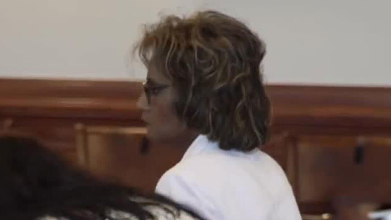 Petite female defendant in a white blazer stands up in court.