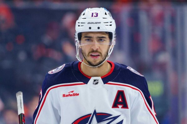 NHL player Johnny Gaudreau looks at the camera in a hockey uniform and helmet