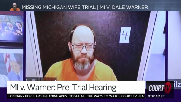 Bearded bald man in orange prison jumper appears for a Zoom pretrial hearing.