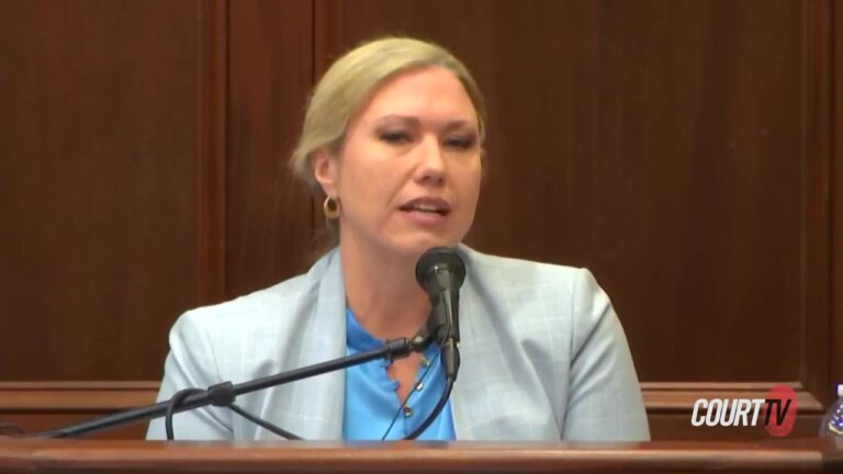 Blonde, professional looking middle aged woman in a suit on the witness stand.