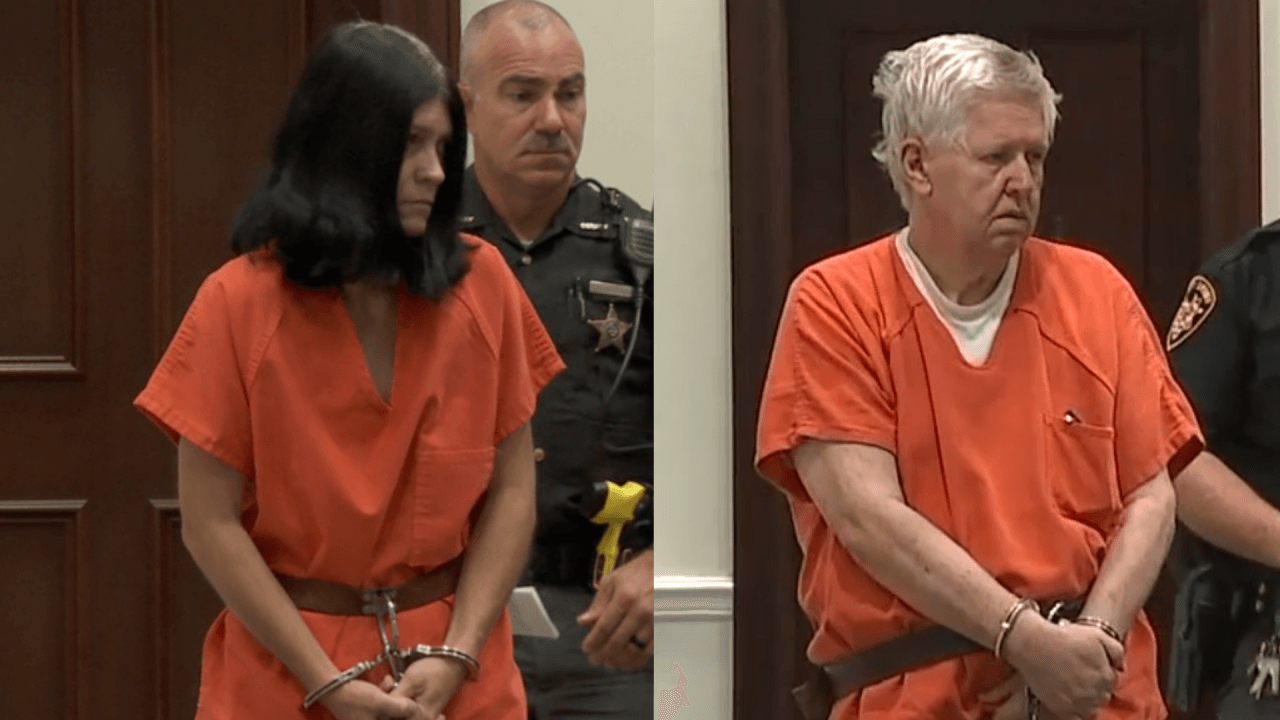 A man and a woman in shackles and prison garb look forlorn.