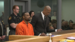 man in orange prison jumper sits at defense table