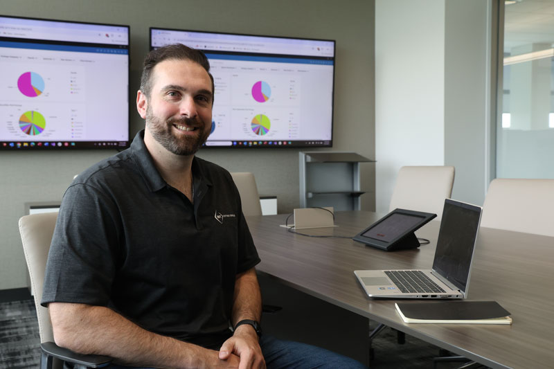 IMT employee sitting with laptop in front of graphs