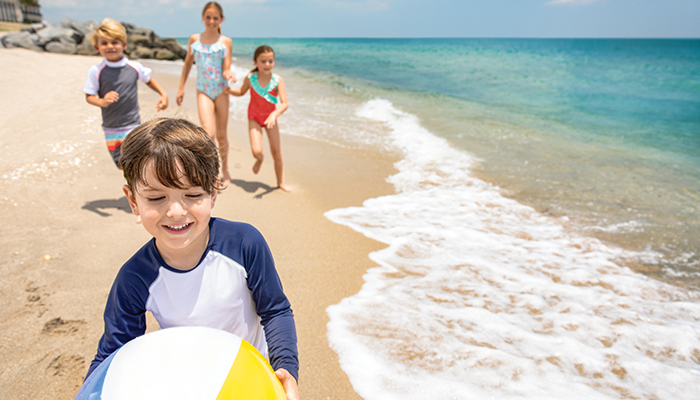 Children walking along the beach with a beach ball at The Breakers Palm Beach