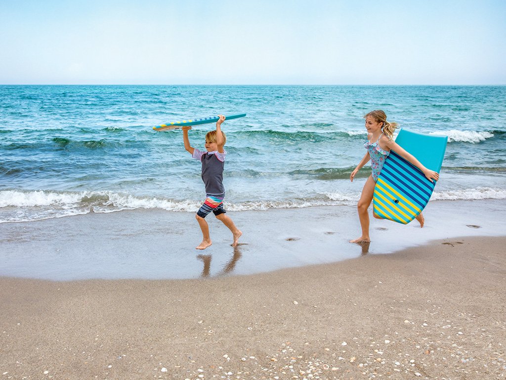 Children walking along the beach with boogie boards at The Breakers Palm Beach