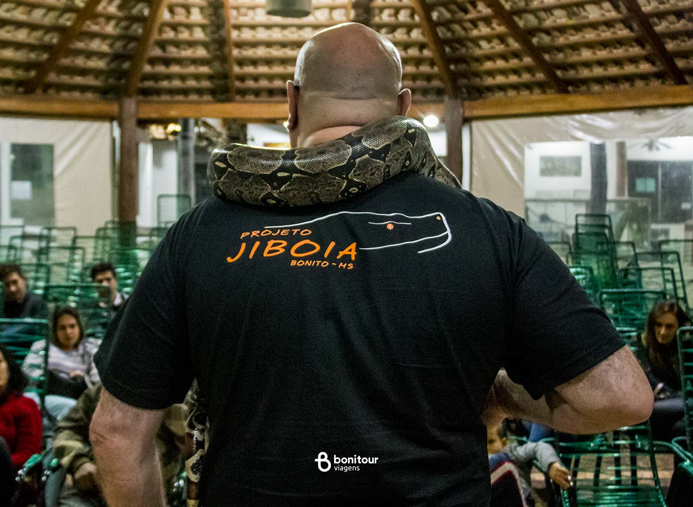 Pessoa de costas segurando serpente jiboia nos ombros