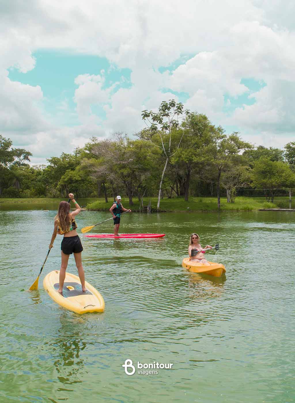 Pessoas em bote e stand up paddle na água com natureza ao fundo