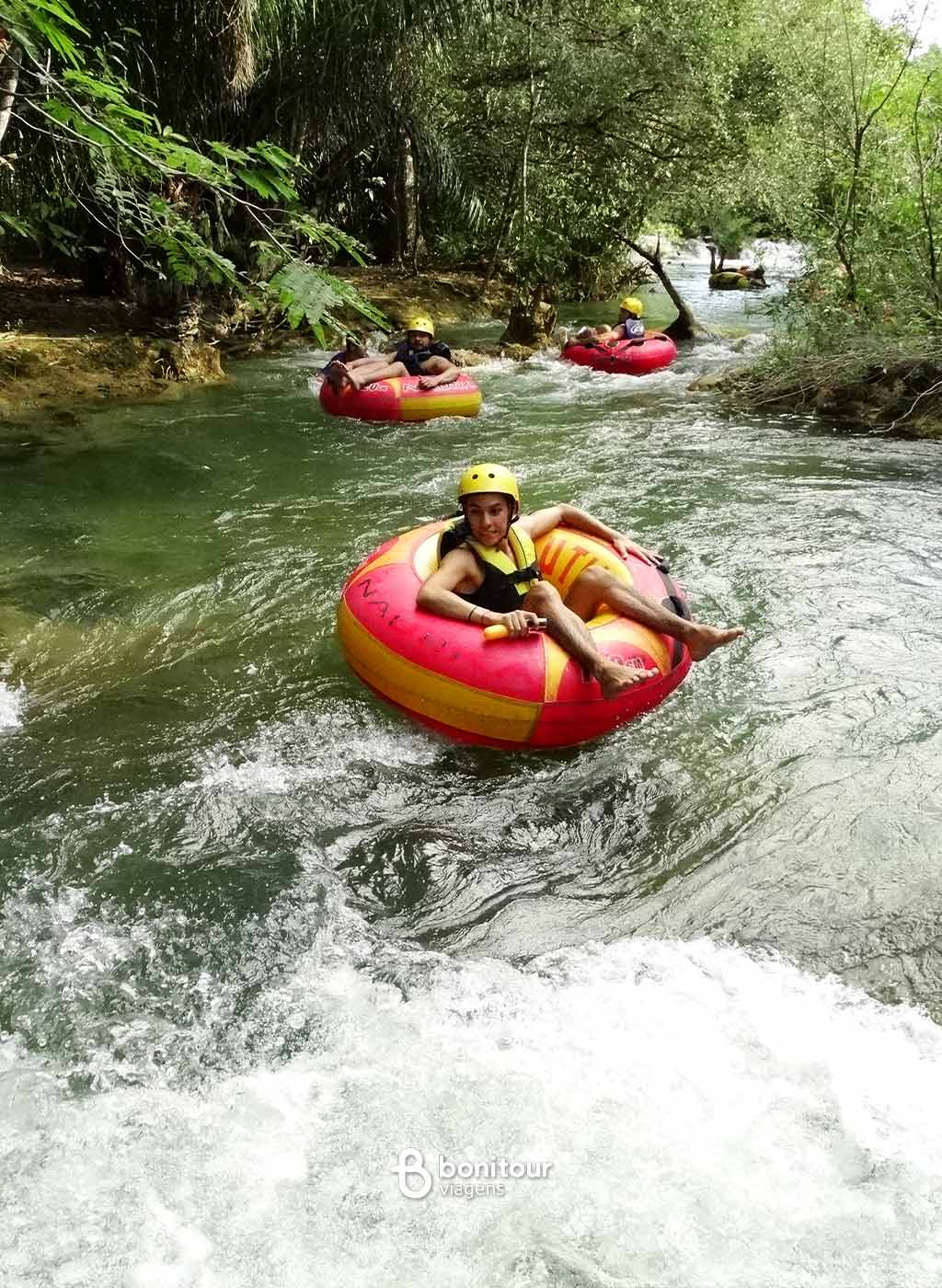 Pessoas descendo de boia cross em queda da água com equipamento de proteção.