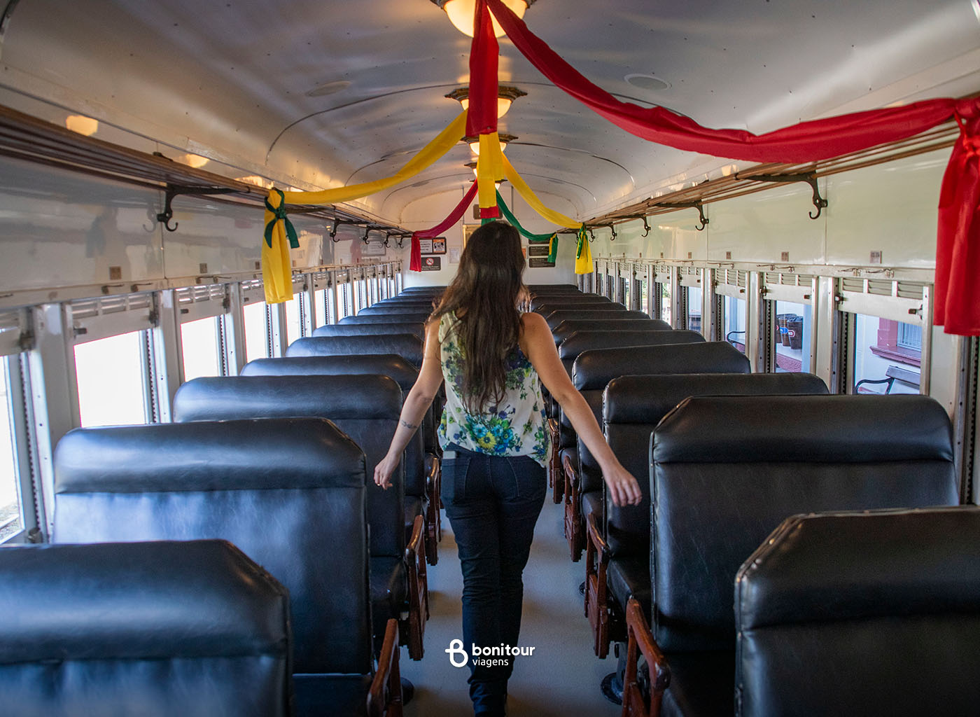Pessoa andando entre as poltronas vazias de vagão do trem Maria Fumaça