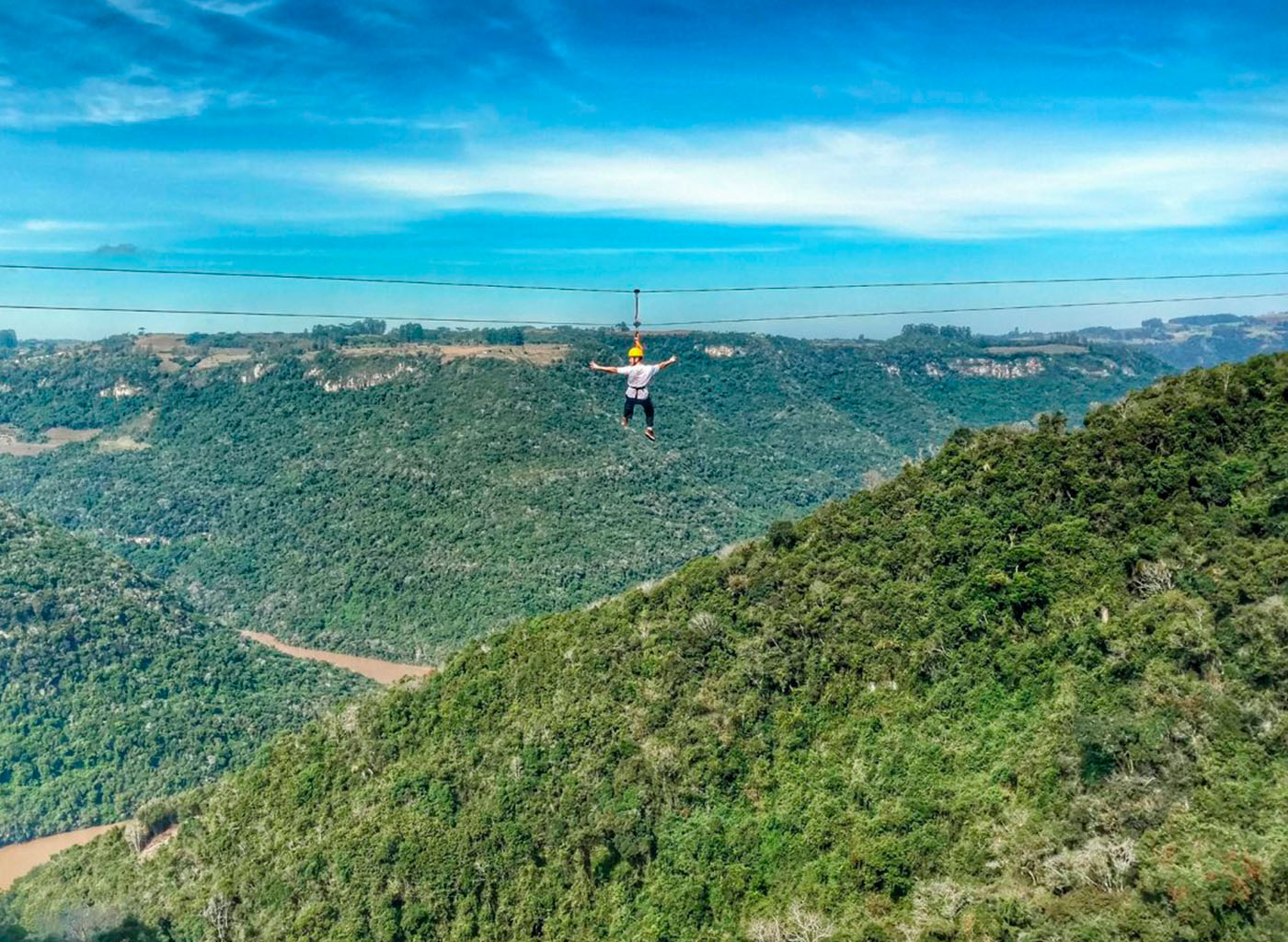 Pessoa descendo de tirolesa com morros ao fundo