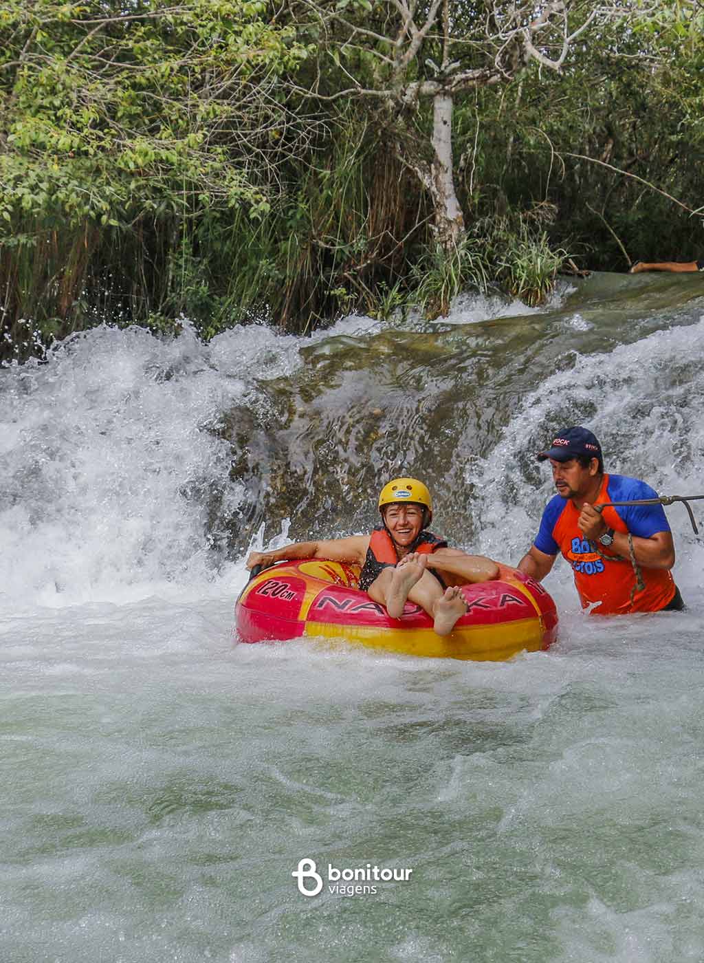 Pessoas descendo de boia cross em queda da água com equipamento de proteção.