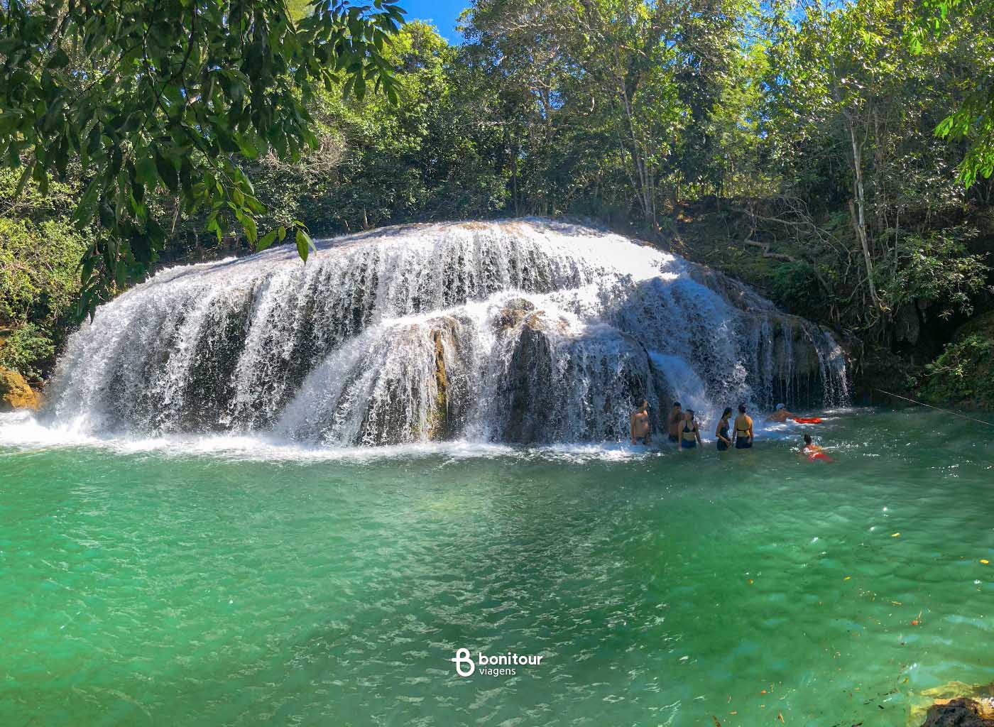 Pessoas nadam em águas de cachoeira da Estância Mimosa em meio à vegetação nativa.