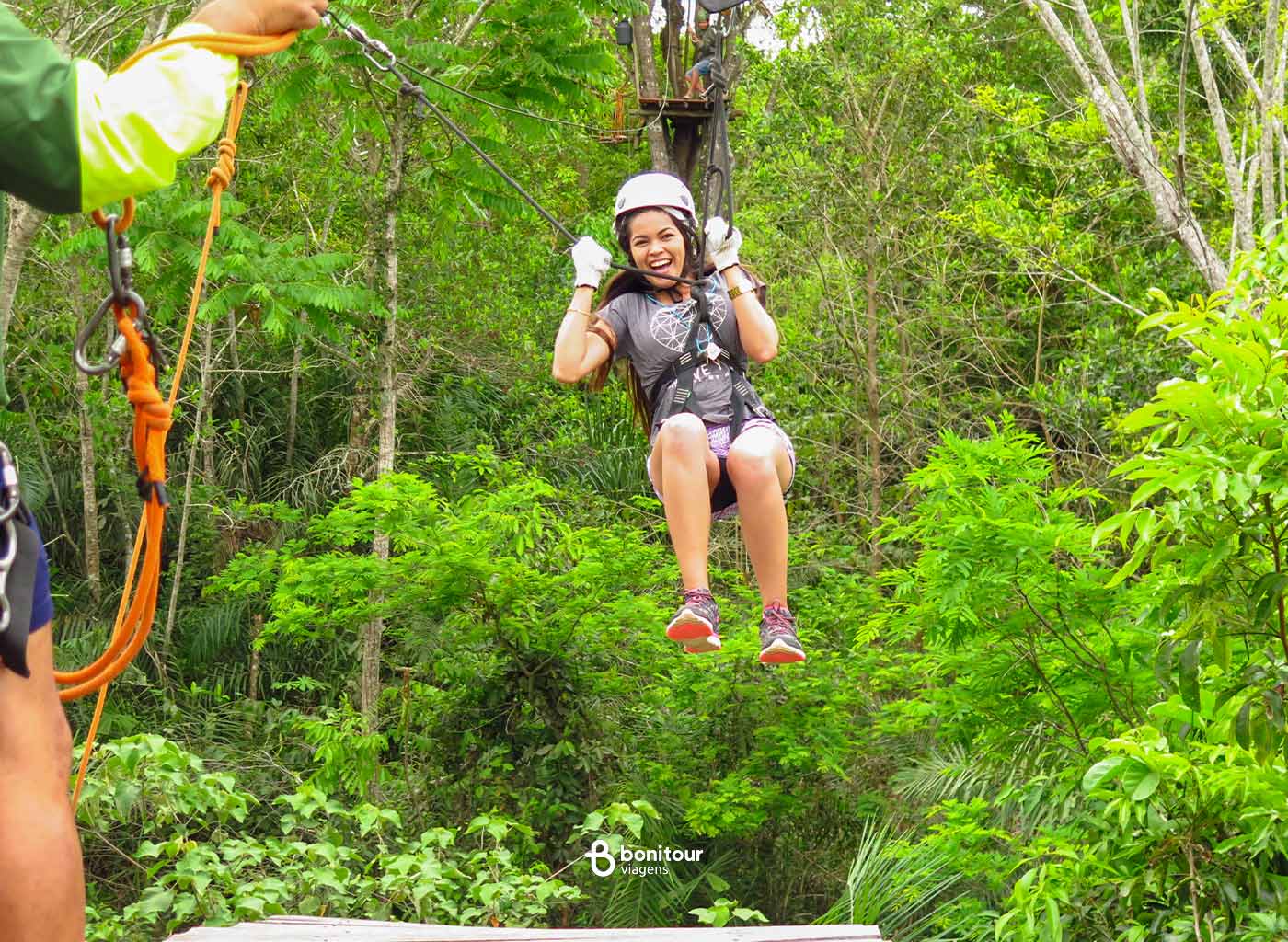 Pessoa com equipamento de segurança, no alto das árvores praticando tirolesa
