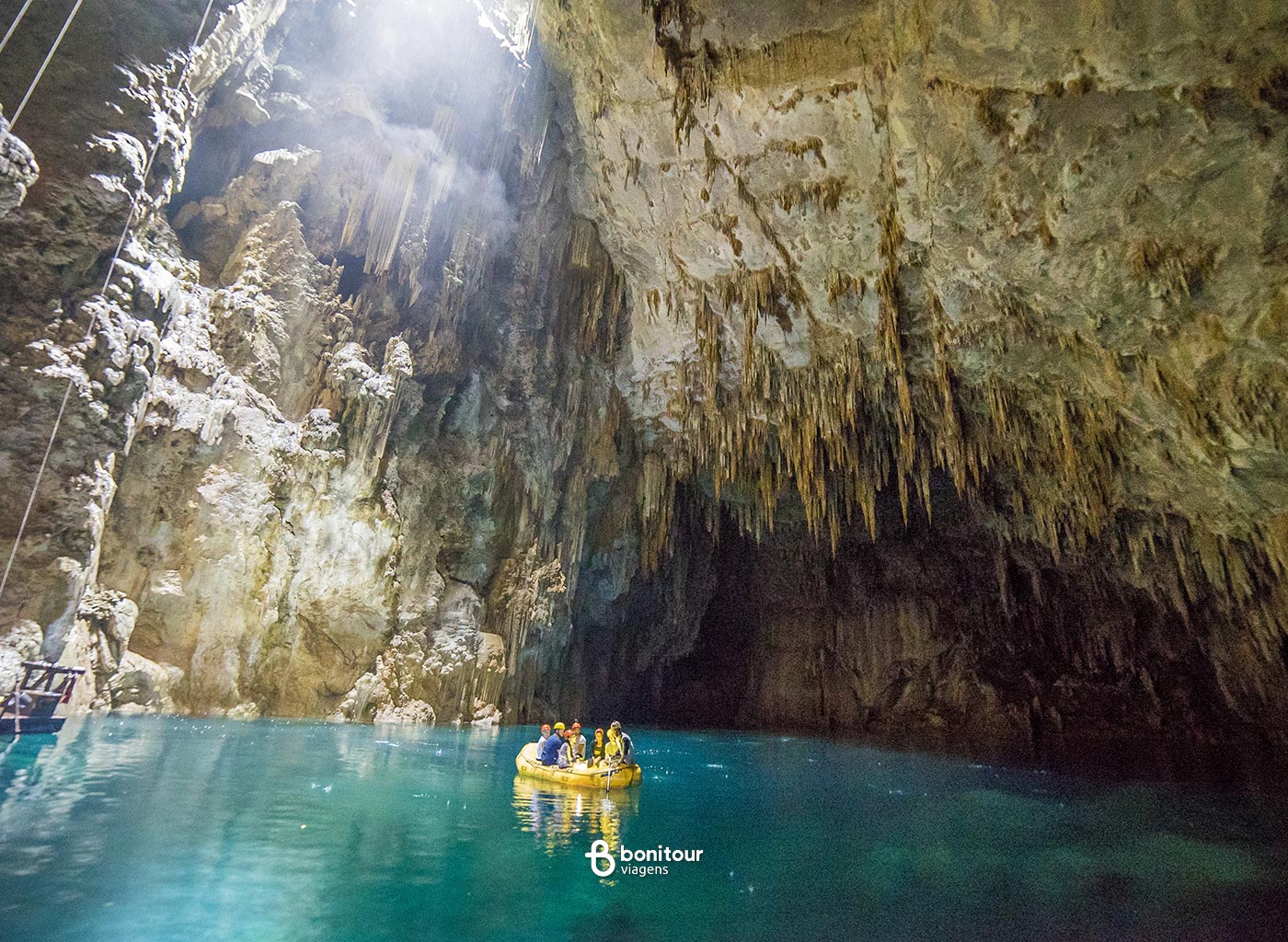 Pessoas navegando de bote dentro do Abismo Anhumas com águas cristalinas e formações rochosas