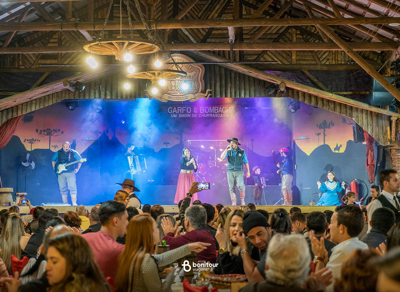 Pessoas jantando com apresentação de fundo do Garfo e Bombacha