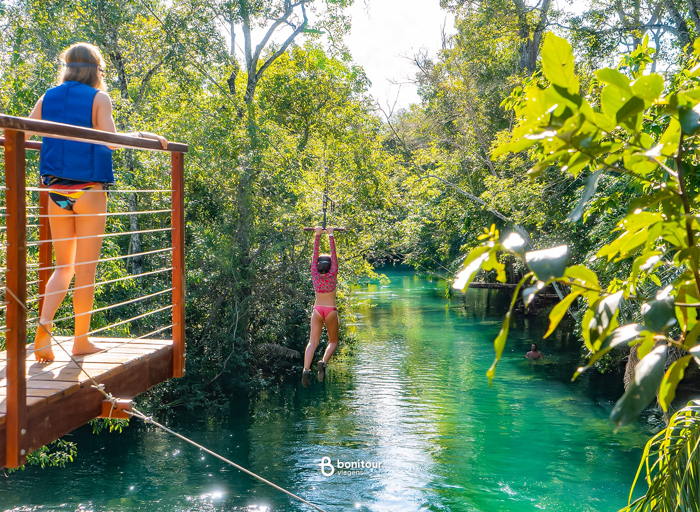 Pessoa descendo de tirolesa em cima de águas cristalinas