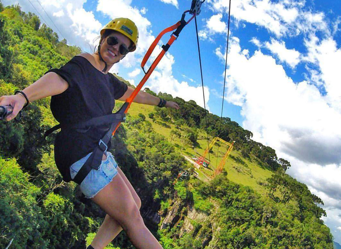Pessoa descendo de tirolesa com morros ao fundo
