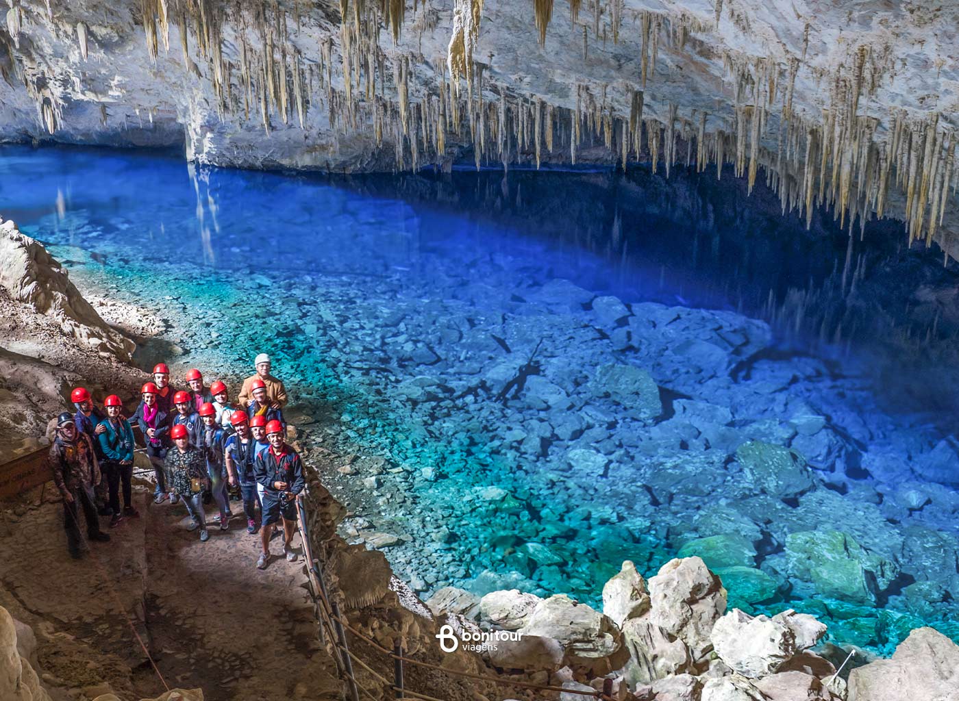 Pessoas contemplando vista da Gruta do lago azul com águas cristalinas azuis e formações rochosas