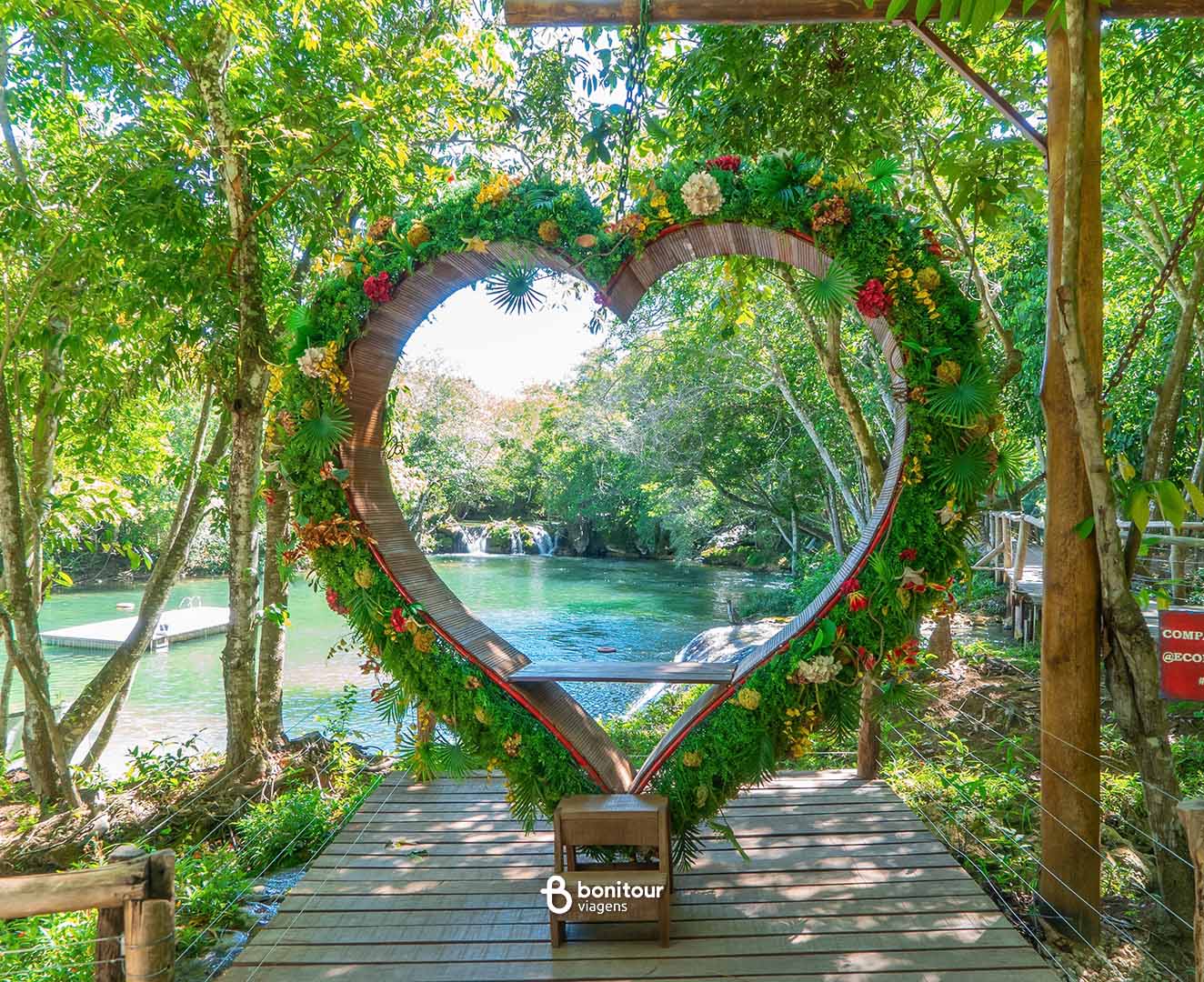 Deck de madeira em formato de coração a beira de águas cristalinas e cachoeira