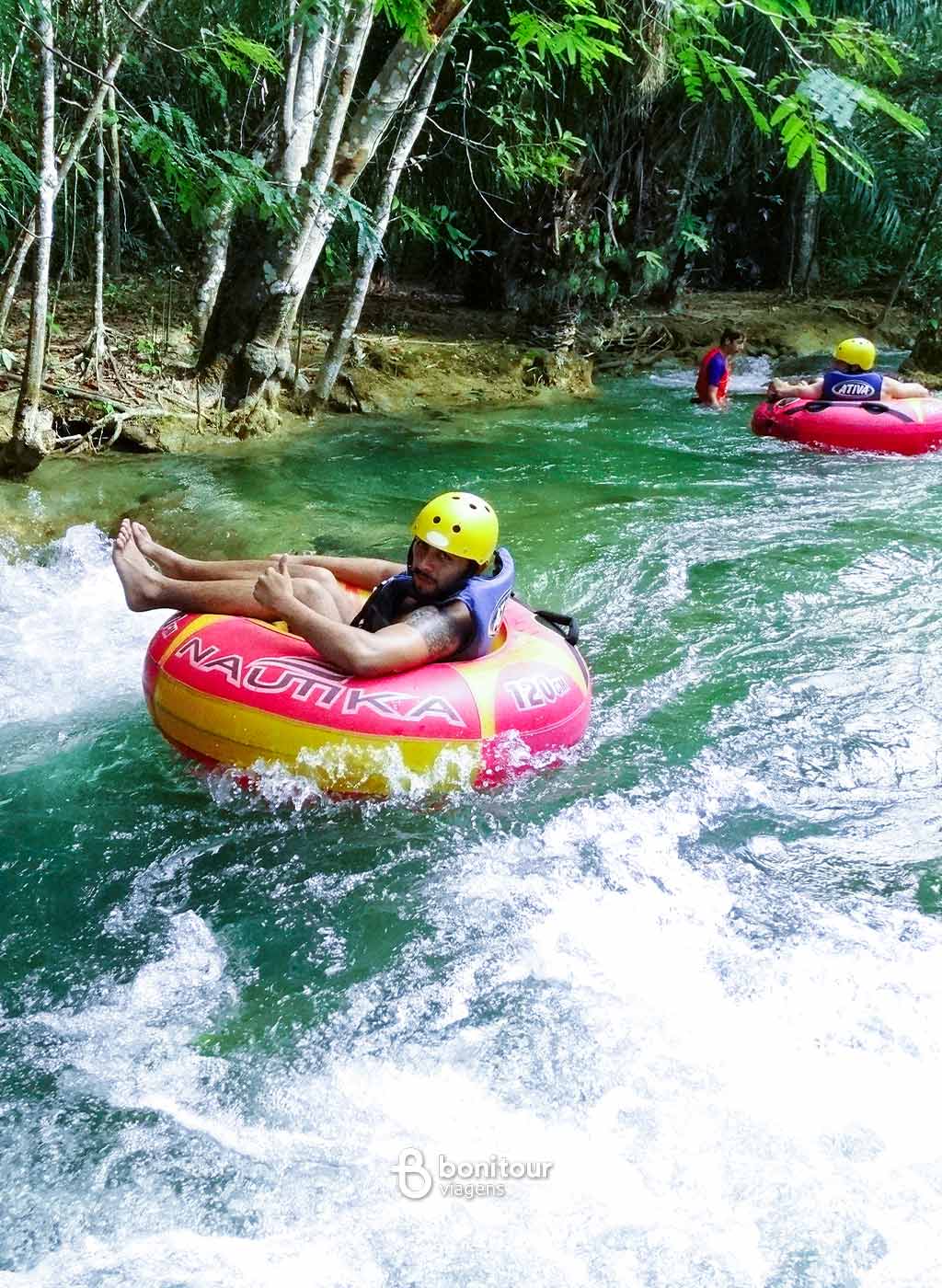 Pessoas descendo de boia cross em queda da água com equipamento de proteção.