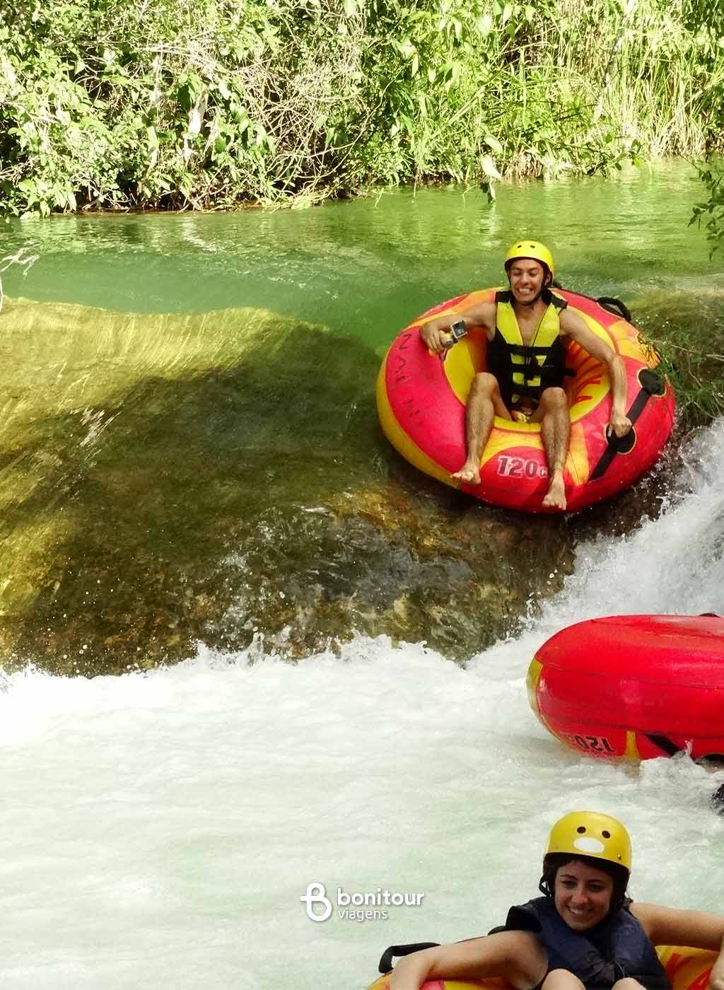 Pessoas descendo de boia cross em queda da água com equipamento de proteção.